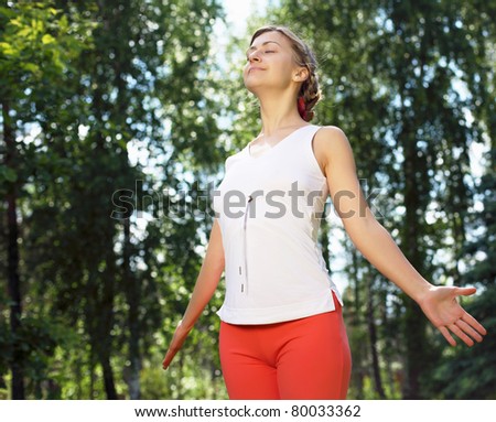 Young girl in a white shirt and red pants doing sport exercises in nature