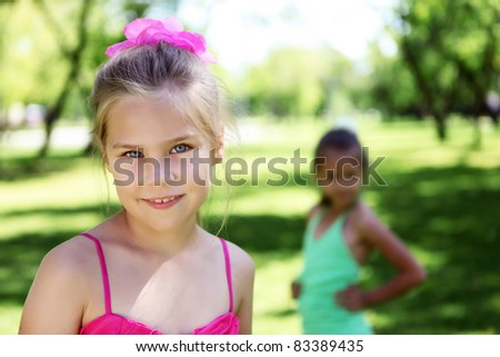 Little girl in bright wear in summer park with friends on the background