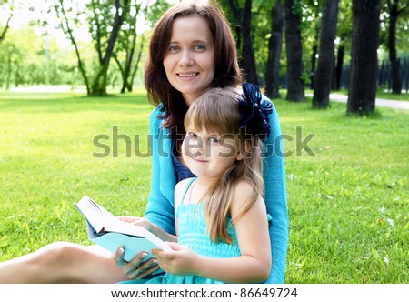 Portrait of little girl reading a book in the park with her mother