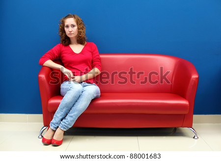 Portrait of young woman sitting on red sofa against blue wall