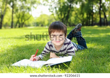 Portrait of a boy lying on the grass with a book in the park