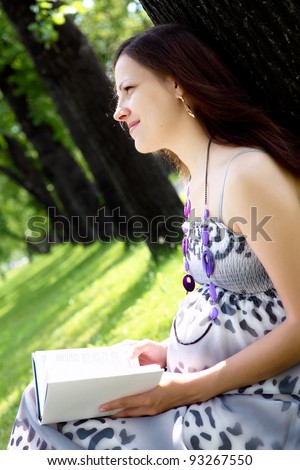 Portrait of pregnant woman reading a book in the park