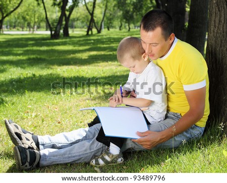 Father with his son reading together in the summer park