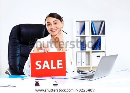 Young woman sitting in office in business wear with sale sign