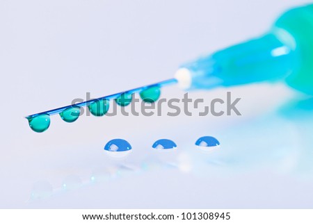 Syringe needle with green fluid drops on droplets water background, macro view
