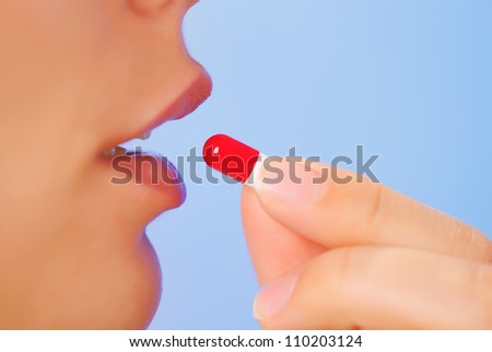Young woman taking red and white bolus (capsule), macro view