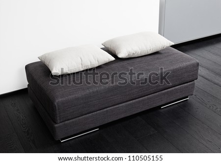 Dark gray padded stool with white pillow, detail of modern sitting room interior in black and white