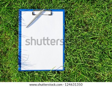 Blue medical clipboard with a pen over lush green grass