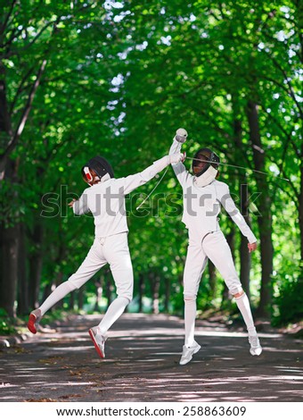 Two rapier fencer women fighting over park alley, attacking each other in jumping
