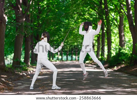 Two rapier fencer women fighting over park alley, attacking each other in jumping