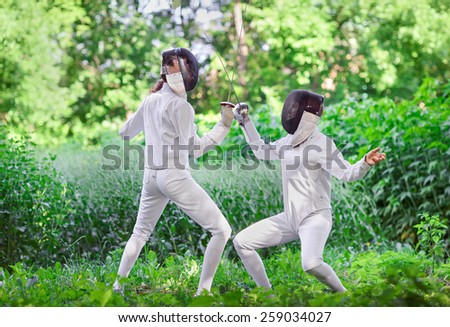Two rapier fencer women fighting over beautiful nature park background