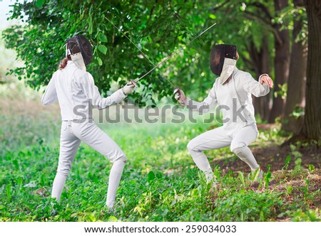 Two rapier fencer women fighting over beautiful nature park background