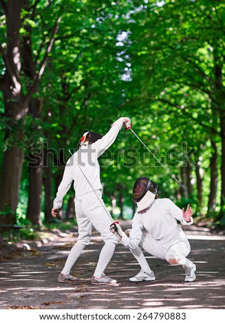 Two rapier fencers women fencing on park path