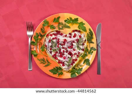 Valentine\'s day salad with beef tongue, onion and apple in heart shape on red table-cloth decorated with greens and  pomegranate seeds