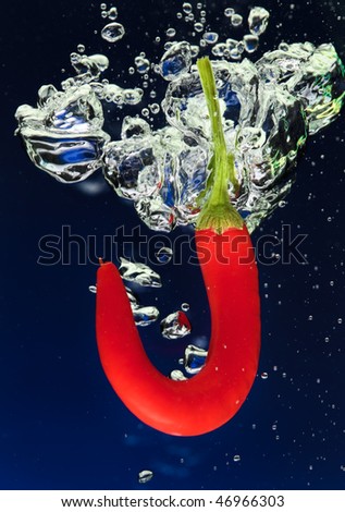 Chilli pepper falling in water on blue with air bubbles