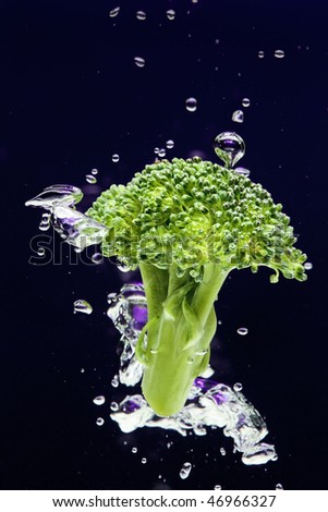 Green broccoli falling in water on blue with air bubbles