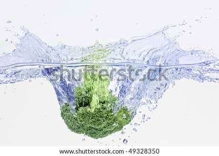 Green broccoli falling in water on white with air bubbles
