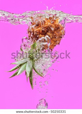Small pineapple falling in water on purple with air bubbles