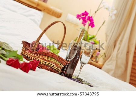 Roses, fruits basket and wine glasses on tea-tray in the bed