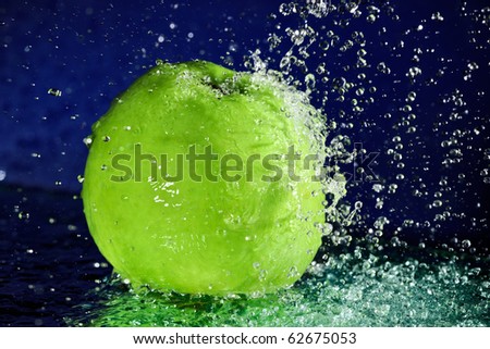 Whole green apple with stopped motion water drops on deep blue