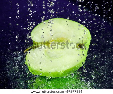 Half of green apple with stopped motion water drops on deep blue