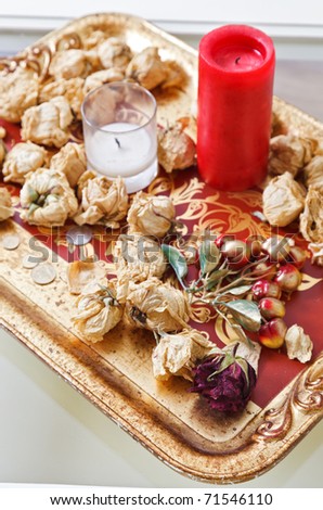 Still life with red candle and dried rose flowers on a gold tray
