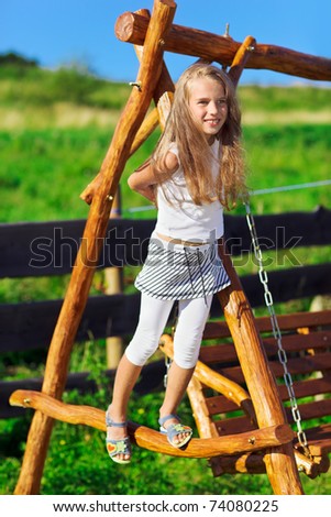 Cute little girl with blond long hair playing on wooden chain swing in rural playground