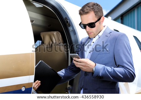 Man with mobile phone and tablet standing in door of small jet plane