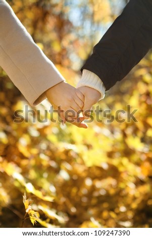 Young couple holding hands in the autumn forest. Close up