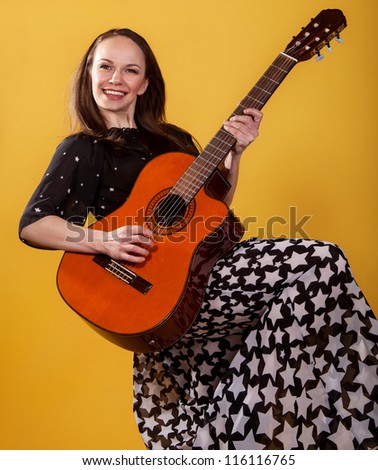 Brunette guitar player woman in long dress on the yellow background