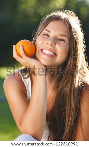 Beautiful young girl with open smile holding orange in summer park