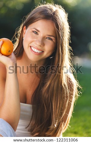 Beautiful young girl with open smile holding orange in summer park