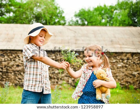 Little boy gives flowers to the little girl near the country house