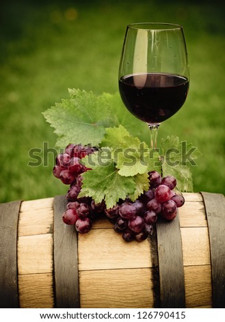 One glass of red wine and green leaves of the grape on the wine barrel. Close up