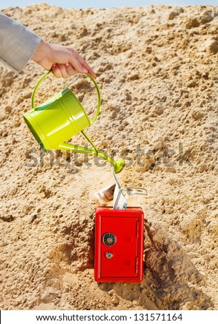Hand of a businesswoman watering a money in safe in a desert. Concept