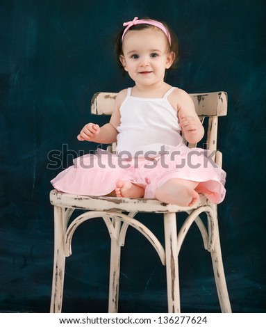 Portrait of the one year old baby on the chair wearing ballet suit indoor