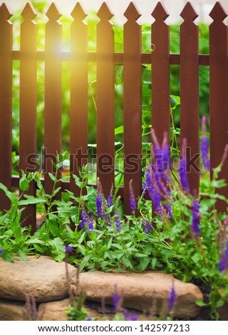 Wooden fence over the courtyard with flowers and sun