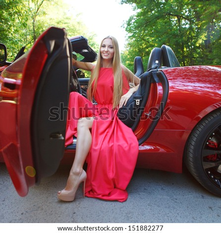 Beautiful blond young woman in red dress siting in a  sports car