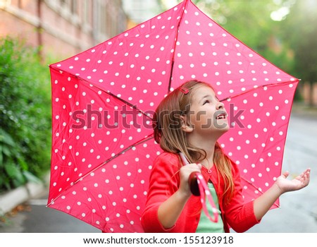 Child with polka dots umbrella wearing red rain boots jumping into a puddle