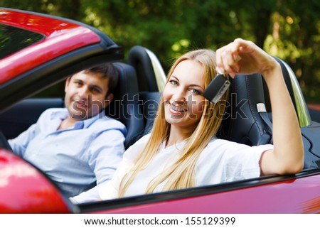 Couple in red cabriolet in a sunny day. Woman holding key