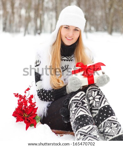 Young smiling woman holding gift decorated with red ribbon outdoors. Winter time