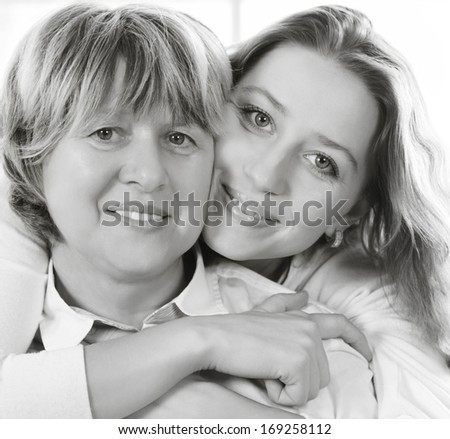 Black and white close up portrait of a mature mother and adult daughter being close and hugging at home being happy and joyful