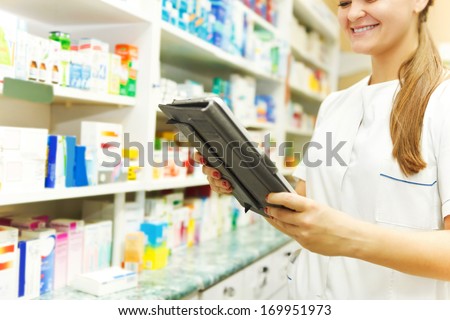 Pharmacist working with a tablet computer in the pharmacy holding it in her hand while reading information