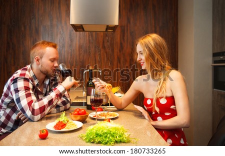 Happy woman eating pasts while man tasting red wine in a kitchen. Couple on the date