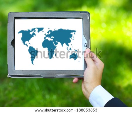 Man holding tablet computer with world map on the green grass background