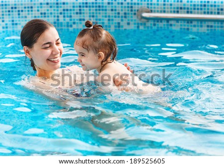 One year baby girl at her first swimming lesson with mother in the pool