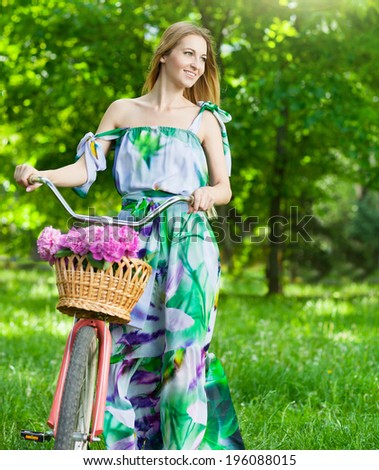 Beautiful woman wearing a nice dress having fun in the city with bicycle carrying a beautiful basket full of peony flowers. Vintage scenery. Pretty girl with retro look, bike and basket with flowers