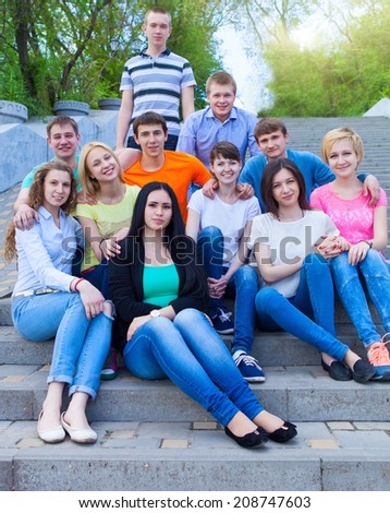 Group of smiling teenagers sitting outdoors. Friendship concept