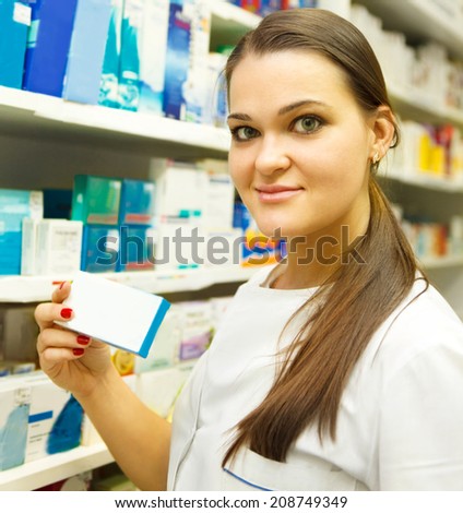 Young female pharmacist showing medicine box at pharmacy counter