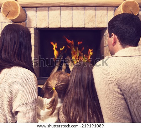 Young happy mother, father and two daughters by a fireplace on Christmas